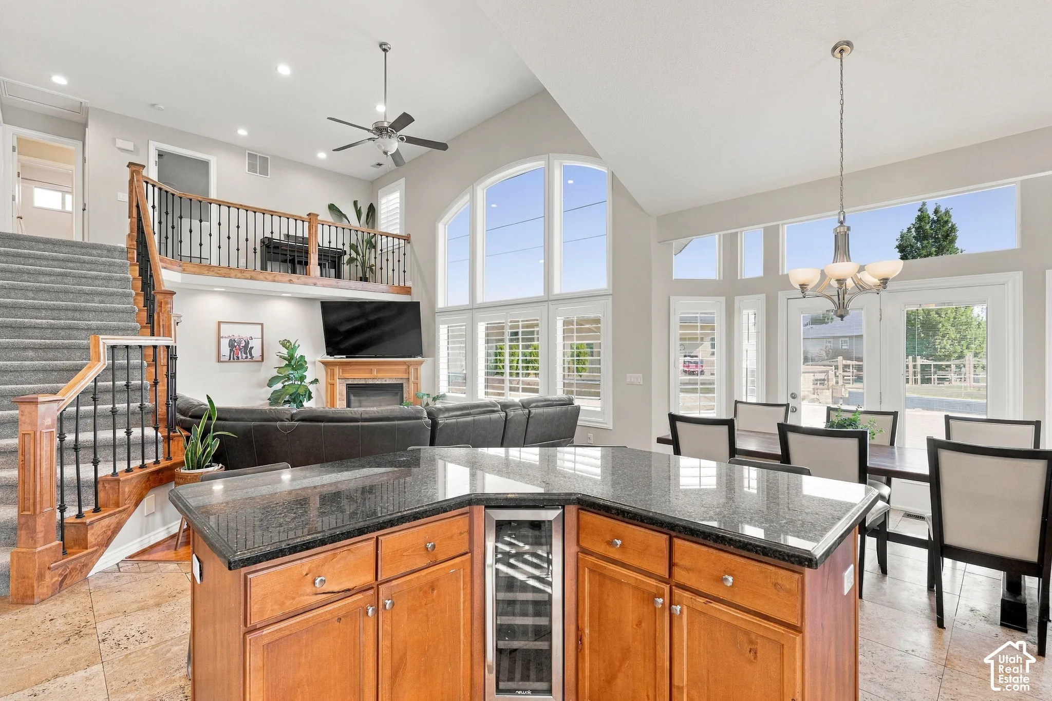 Kitchen island with granite countertops and integrated beverage cooler, vaulted ceilings, two-story great room with fireplace, grand staircase with wrought iron balusters, and multiple windows
