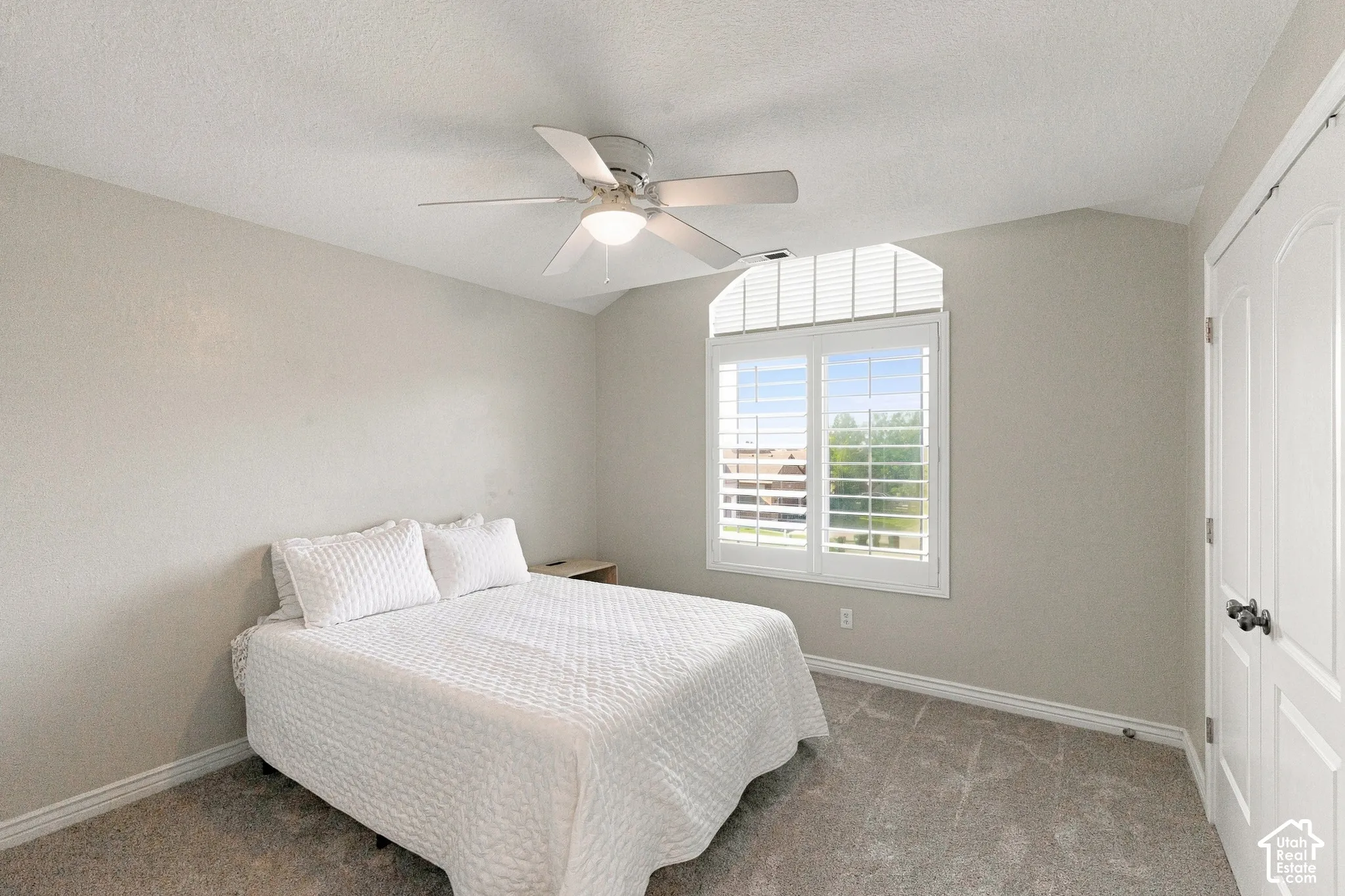 Arched window with plantation shutters, ceiling fan with integrated lighting, paneled door with dark hardware, and neutral-toned carpeting