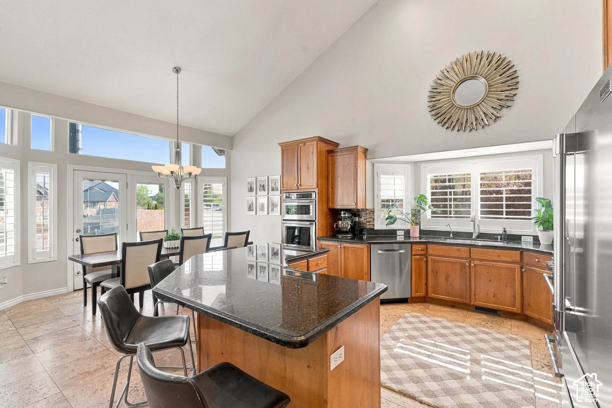 Vaulted ceiling with a contemporary chandelier, stainless steel appliances, wood cabinetry, stone countertops, and tile flooring
