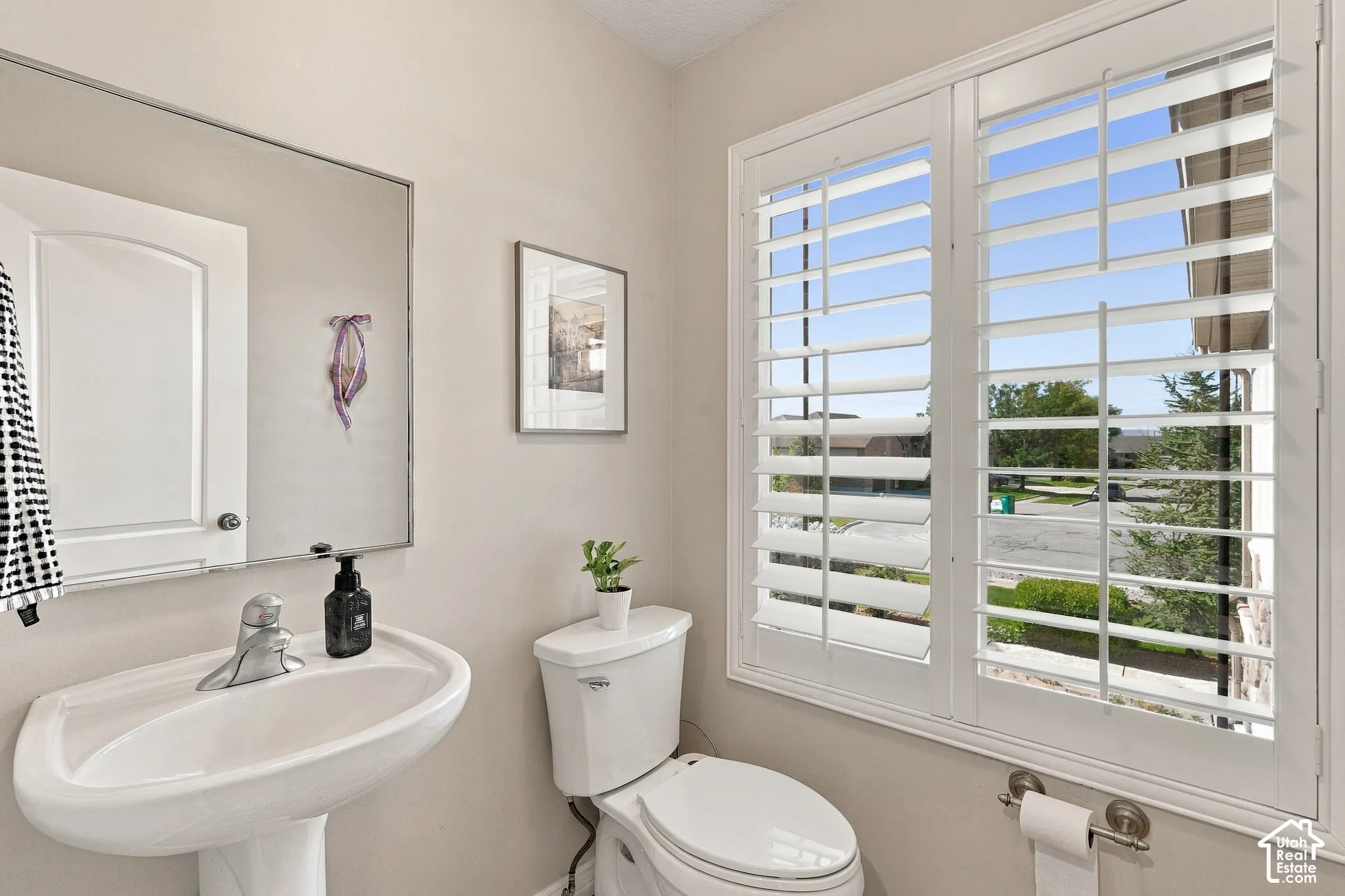 Pedestal sink, wall-mounted mirror, white window shutters, and white toilet