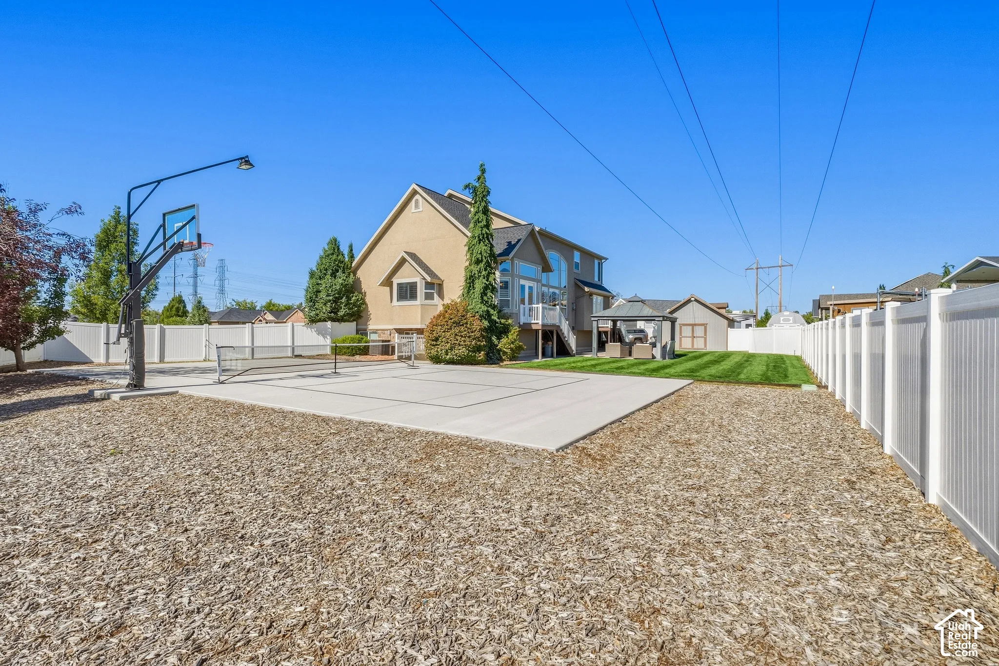Spacious backyard featuring a concrete sport court with a basketball hoop, wood chip landscaping, and a white privacy fence