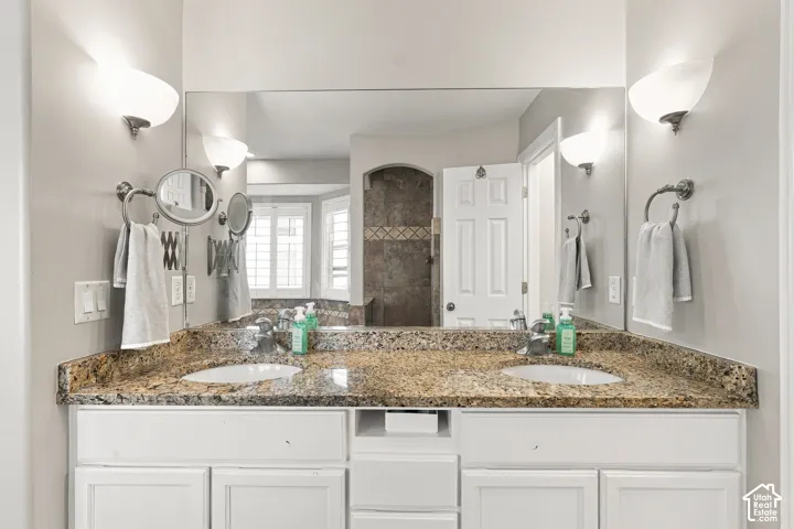 Double vanity with granite countertop, integrated sinks, white cabinetry, and wall-mounted sconces