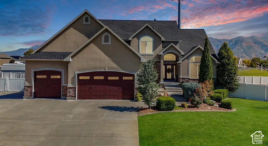 Stucco exterior with stone accents, dark garage doors with window inserts, established landscaping, and a mountain backdrop
