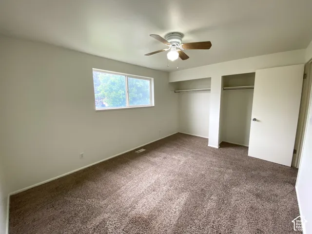 Carpeted room featuring a ceiling fan with integrated lighting, a double window, and two closet openings