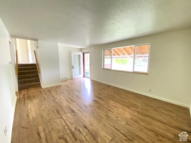 Hardwood-finish flooring, white walls, large window, glass-panel entry door, and carpeted stairs with wooden handrail