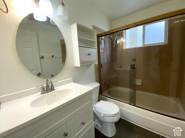 Vanity with integrated sink and brushed nickel faucet, large oval mirror, built-in shelving, bath/shower combination with glass enclosure, and dark-toned floor tiling