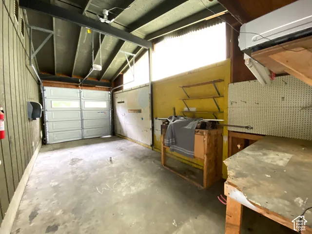 Concrete floor, overhead garage door, built-in shelving, wall-mounted pegboard, wall-mounted air conditioning unit