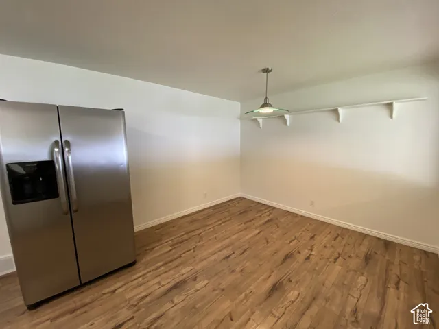 Wood-finish flooring with white baseboards, a stainless steel side-by-side refrigerator, a suspended ceiling light fixture, and a wall-mounted display shelf