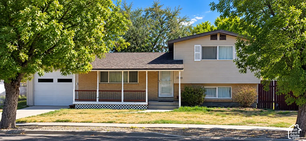 Multi-level residence featuring a covered front porch, attached garage with a white door, and a shingle roof