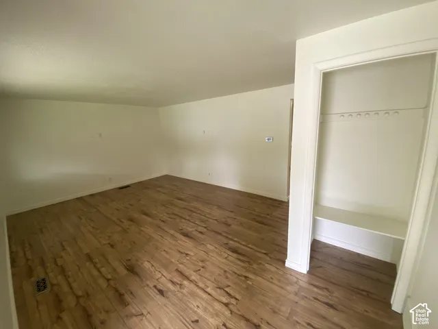 Wood-finish flooring throughout, smooth white ceilings, and a built-in closet with shelving and hanging rod