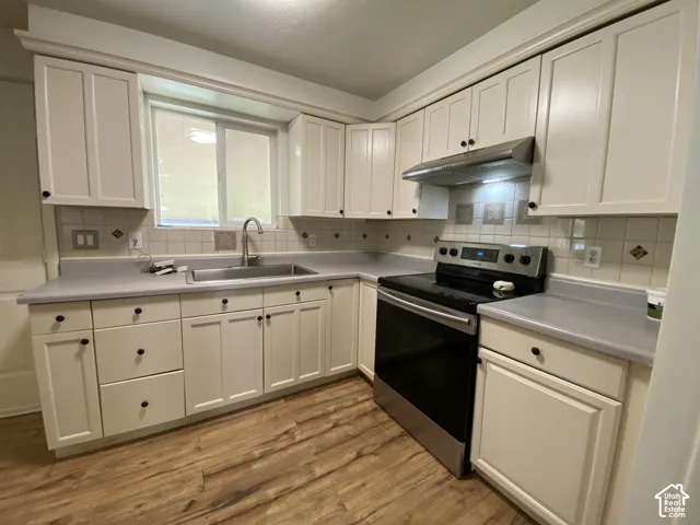 White cabinetry with black hardware, wood-finish flooring, sink with a gooseneck faucet, light-toned countertops, and a tile backsplash