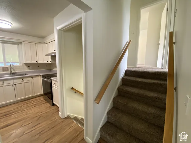 Kitchen with wood-finish flooring, white cabinetry, integrated stainless steel appliances, and a tiled backsplash