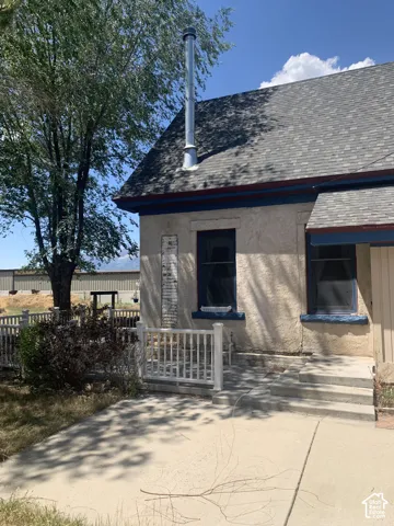 Stucco exterior featuring dual-pane windows, a composite shingle roof, and a metal chimney