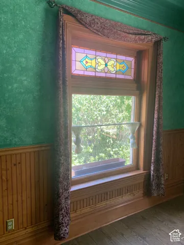 Stained glass transom window, rich wood window trim, wood-paneled wainscoting, wood-finish flooring, and ornate ceiling trim