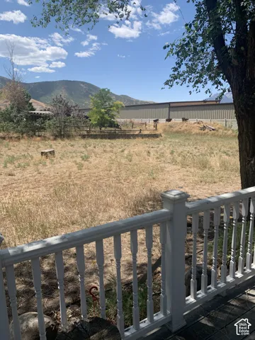 Expansive outdoor area with a white baluster railing, mature trees, and mountain scenery