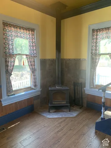 Wood-finish flooring, built-in wood-burning stove with tile hearth, wainscoting, and window trim