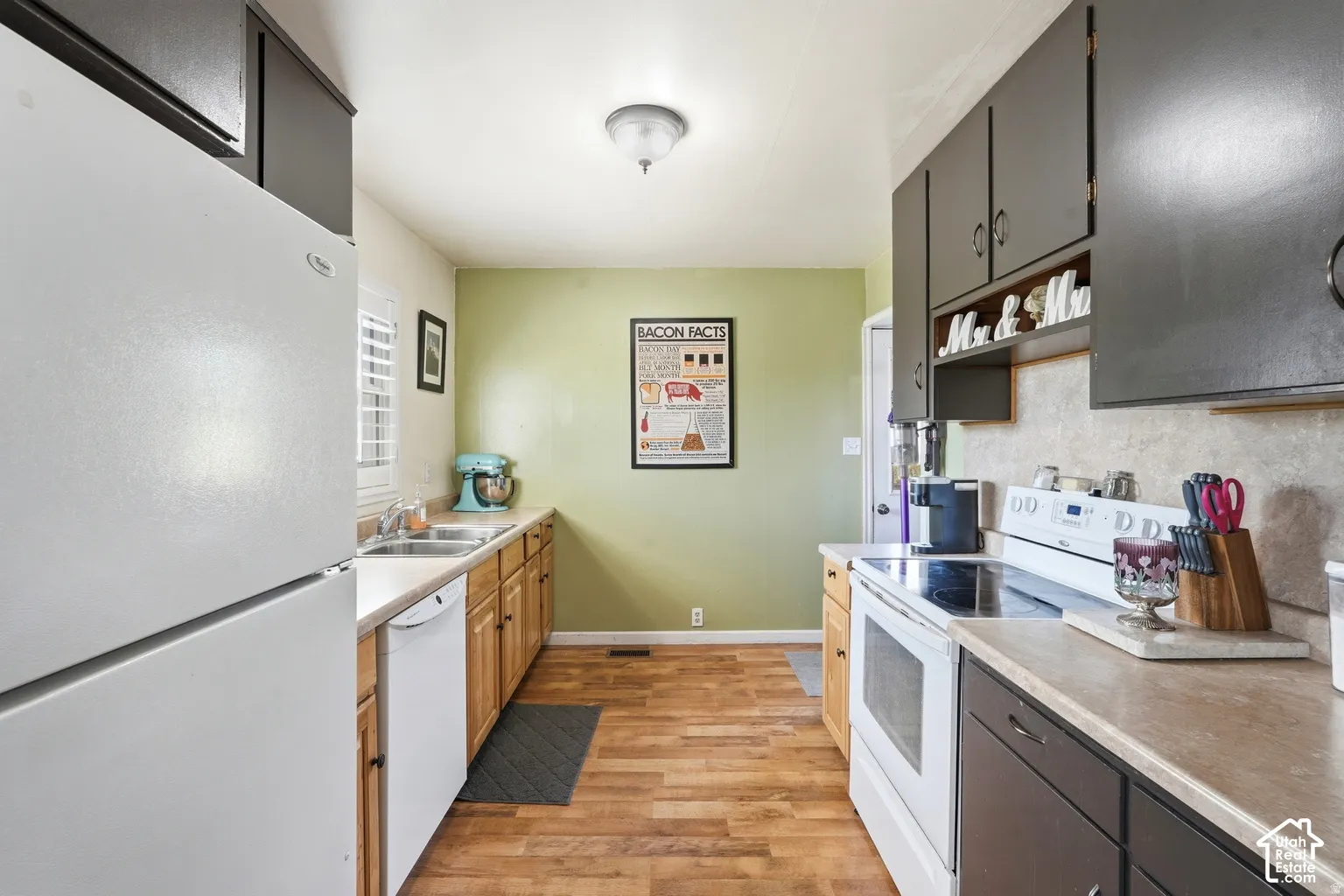 Galley kitchen featuring wood-finish flooring, light-toned countertops, contrasting dark and light wood cabinetry, and a double-basin sink