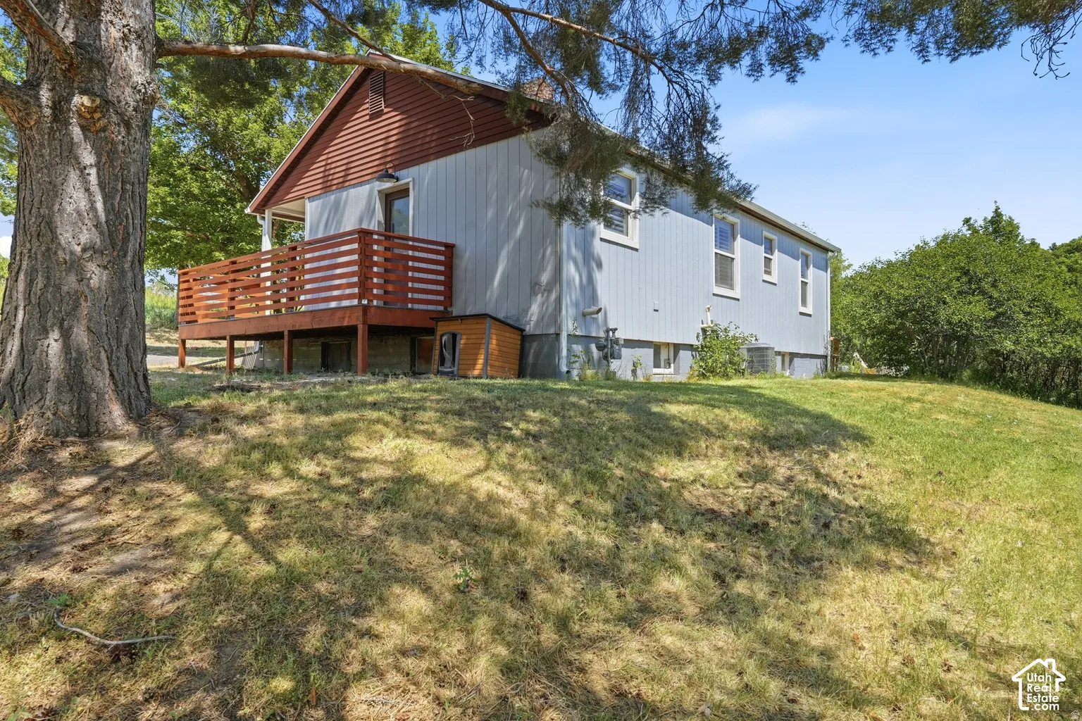 Exterior featuring a wooden deck with railing, light blue siding, and a sloped lawn
