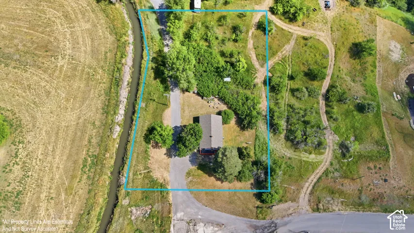Expansive property with a single-story residence, gravel driveway, mature trees, and a bordering canal
