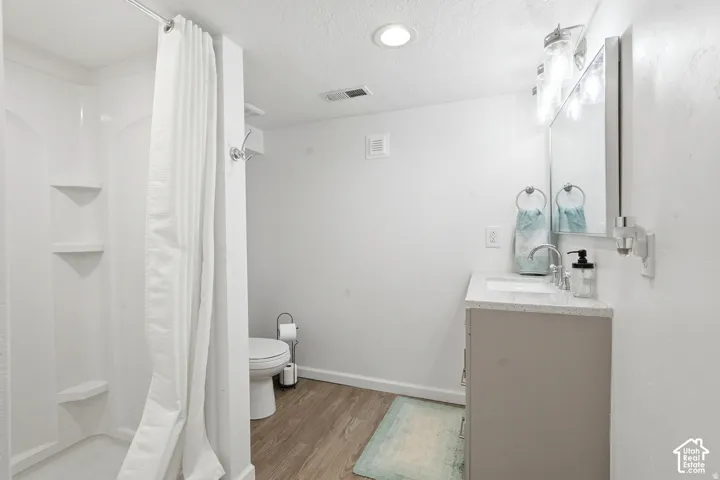 Shower with built-in shelving, wood-finish flooring, single vanity with light-toned countertop, wall-mounted mirror, and overhead lighting