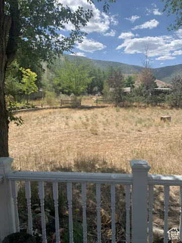 Mountain backdrop with a clear sky, an expansive open area, wood fencing, and mature trees