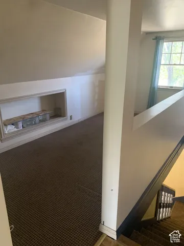 Built-in wall niche, sloped ceiling, patterned carpet, window with natural light, and painted railings