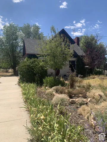 Gabled roofline, red brick chimney, stucco exterior, mature surrounding trees, and a concrete pathway
