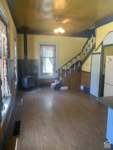 Wood-finish flooring, staircase with wood newel posts and railings, wood-paneled walls, wood-burning stove, and a decorative ceiling