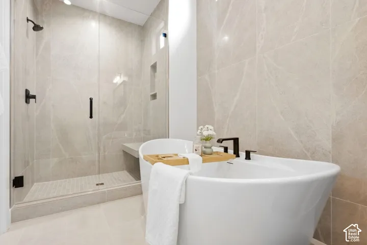 Freestanding soaking tub with a matte black faucet, glass-enclosed shower with a built-in bench, and large format wall tiling