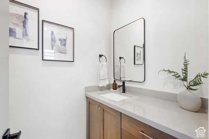 White walls featuring a wood-finish vanity with an undermount sink, light-toned countertop, and a rectangular mirror with a black frame