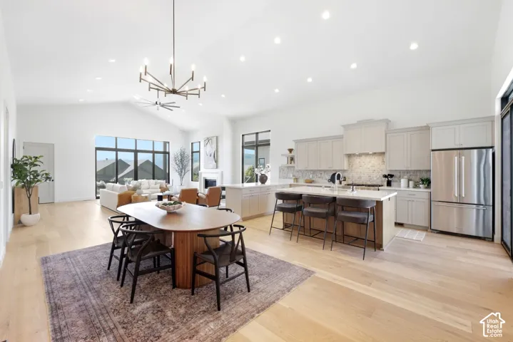 Vaulted ceiling with recessed lighting, light wood-finish flooring, full-height windows, kitchen island with counter seating, and stainless steel appliances