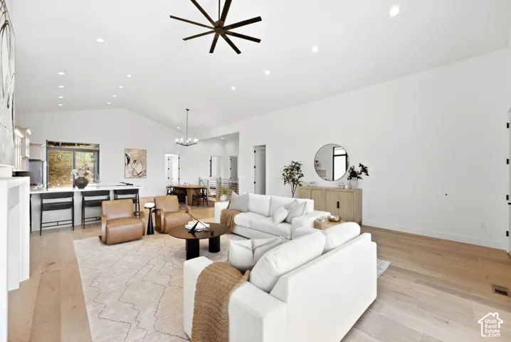 Vaulted ceilings with recessed lighting, light wood-finish flooring, white walls, and a kitchen island with seating