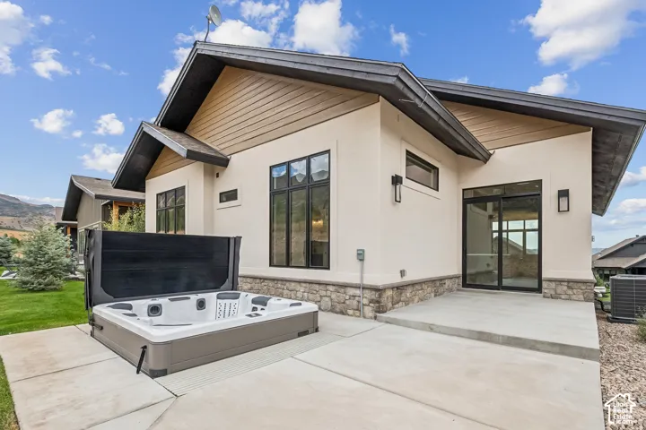 Spacious concrete patio with a built-in spa, complemented by a stucco exterior with stone accents, black-framed windows, and a sliding glass door