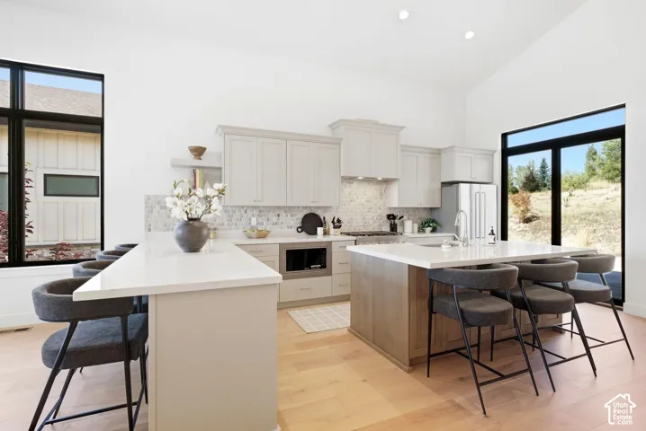 Vaulted ceiling, light wood-finish flooring, dual kitchen islands with light countertops, light-toned cabinetry, and a full tile backsplash