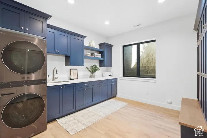 Laundry area featuring blue shaker-style cabinetry, a built-in sink with a gooseneck faucet, white countertop, and wood-finish flooring