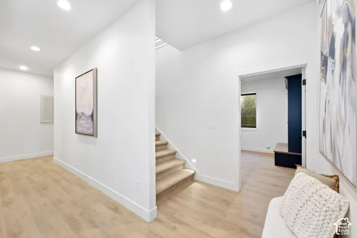 Recessed lighting, wood-finish flooring, staircase with carpeted treads, white walls, and a dark-paneled door