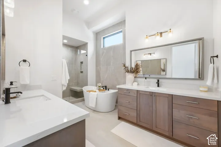 Dual vanities with white countertops, wood-finish cabinetry, a freestanding soaking tub, a walk-in shower with a built-in bench, and large format wall tiling