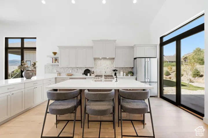Spacious kitchen featuring an expansive island, light wood-finish flooring, white cabinetry, stainless steel appliances, and a large sliding glass door