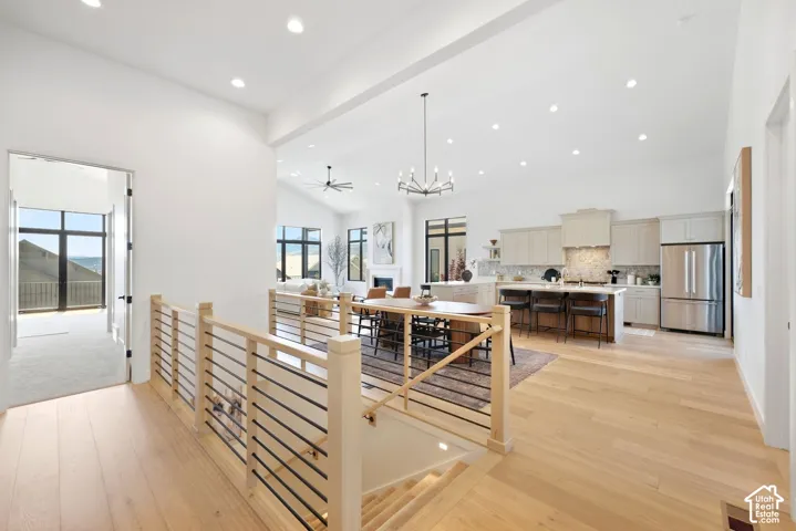 Light wood-finish flooring, staircase with natural wood and black metal railings, recessed lighting, white walls, and a kitchen with stainless steel appliances