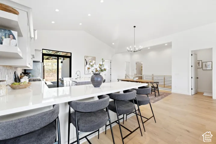 Vaulted ceiling, recessed lighting, expansive island with light-toned countertop, wood-finish flooring, and sliding glass door