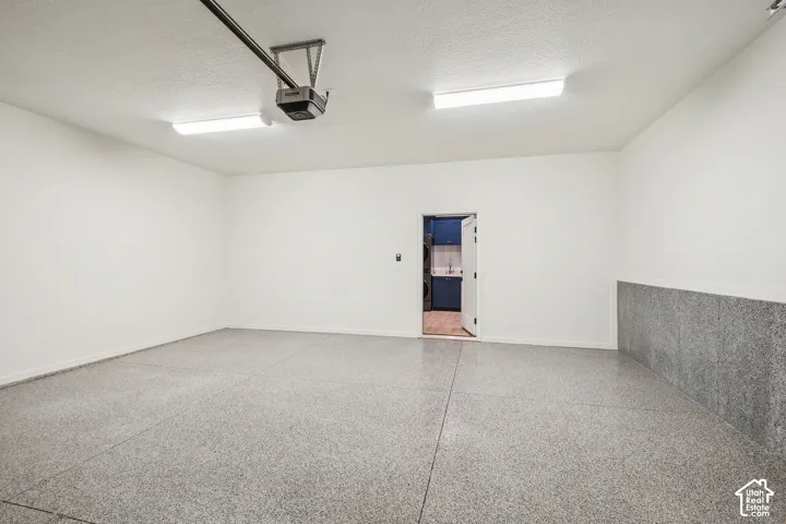 Spacious garage with speckled epoxy flooring, overhead fluorescent lighting, and a white interior door