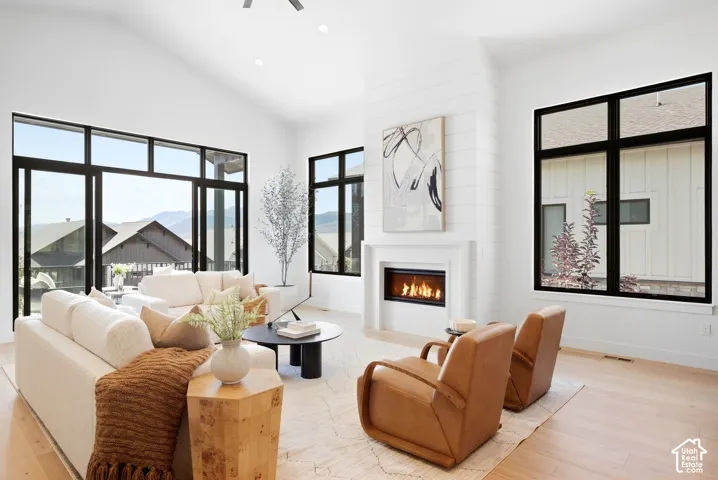 Vaulted ceilings, a built-in fireplace with a shiplap accent, light wood-finish flooring, and large black-framed windows