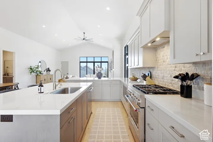 Expansive kitchen featuring a large island with an undermount sink, stainless steel appliances, white cabinetry, and a full tile backsplash