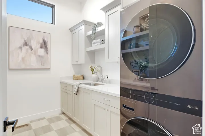 Utility room featuring a built-in sink, white cabinetry with open shelving, and a stacked laundry appliance