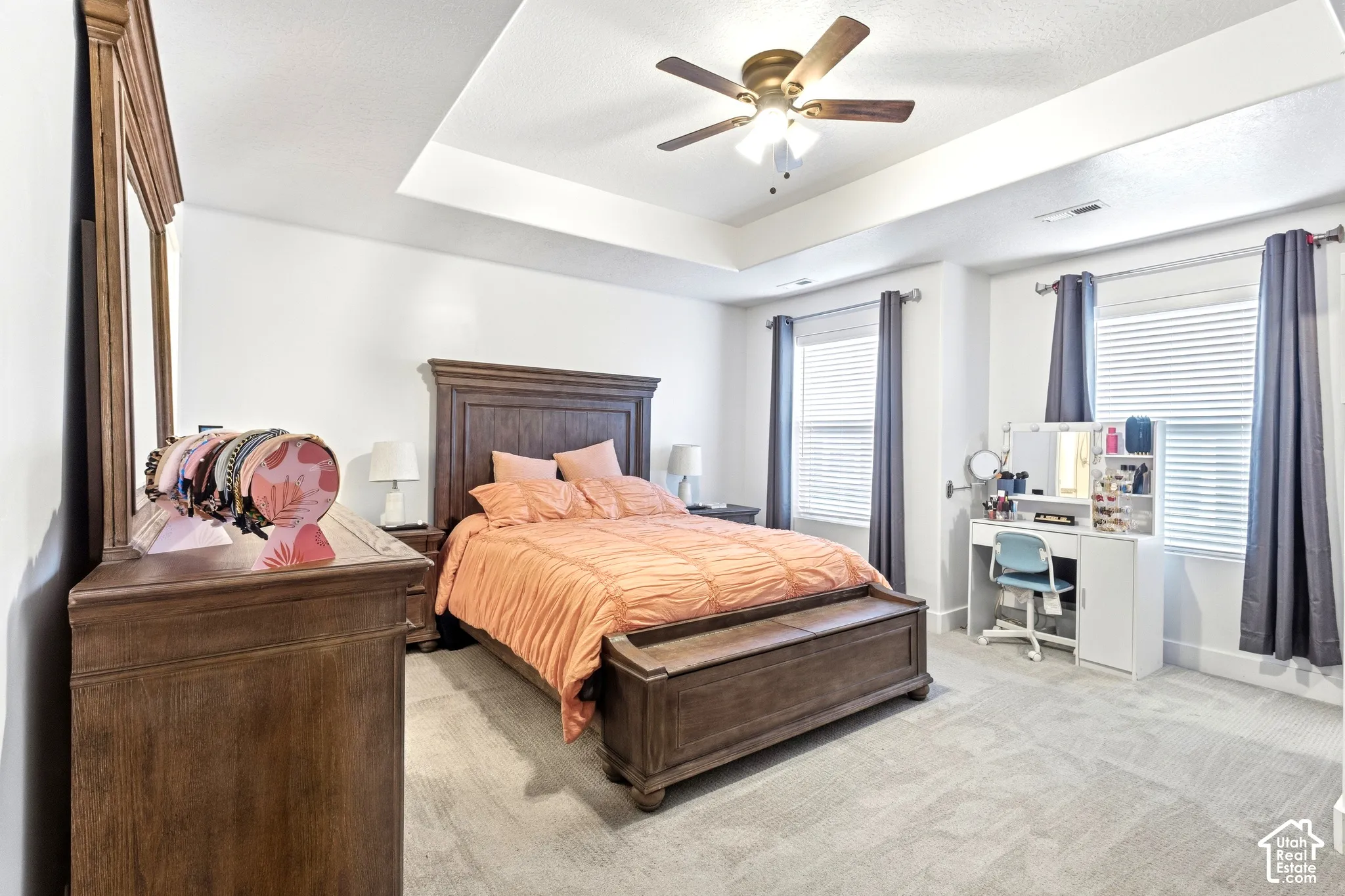 Tray ceiling with a ceiling fan, dual windows with blinds, and light-toned carpeting