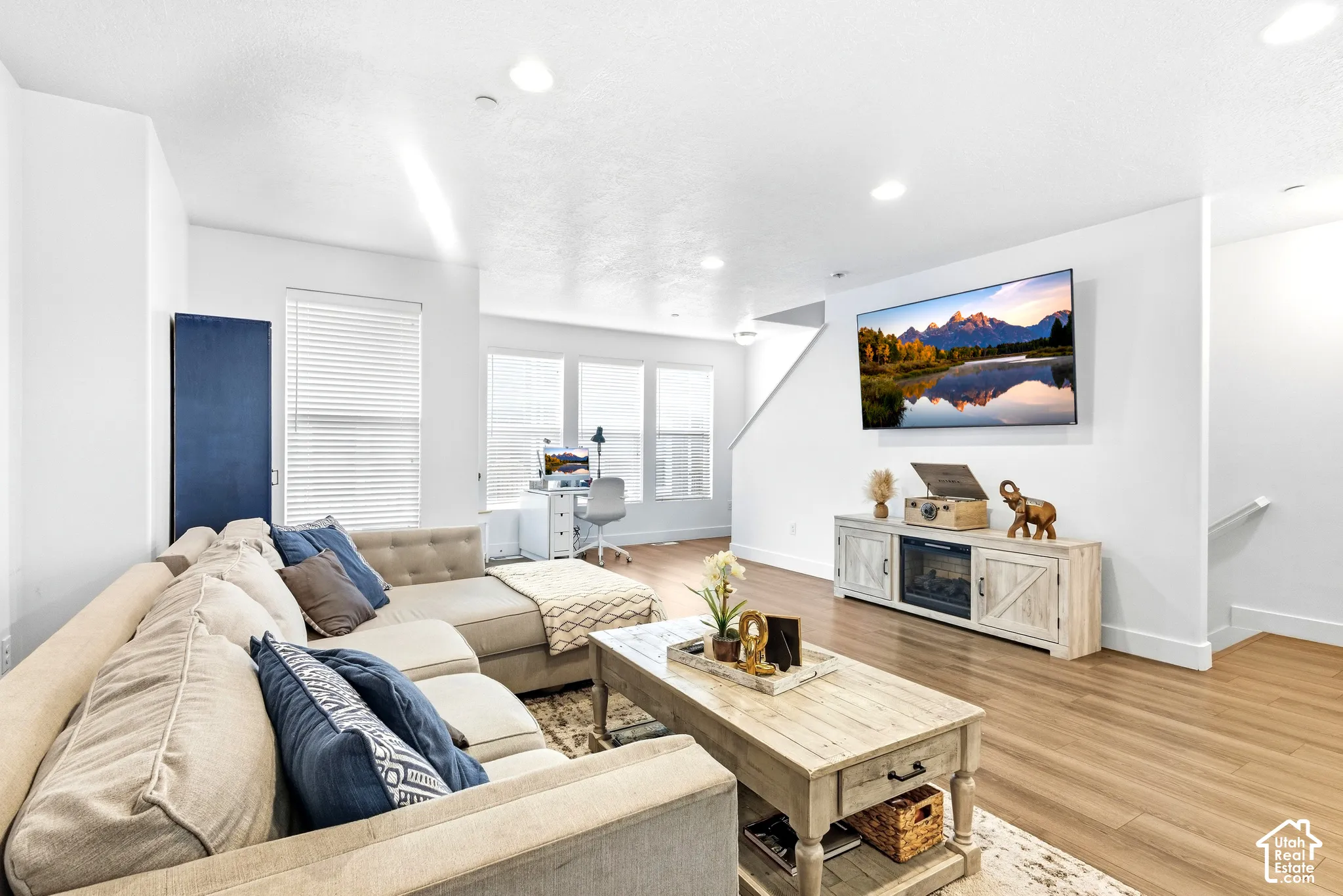 Open-concept living space featuring wood-finish flooring, recessed lighting, and large windows with blinds