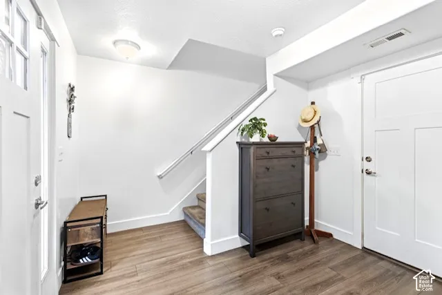 Wood-finish flooring with white baseboards, a white staircase with a metal handrail, and a white interior door with panel details