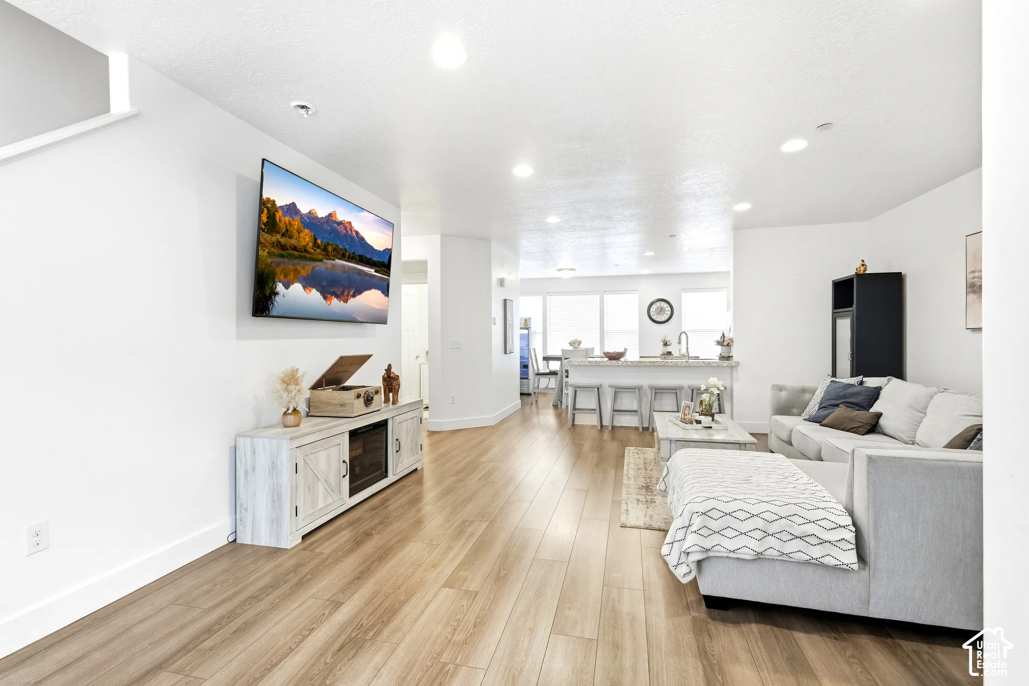 Recessed lighting, wood-finish flooring, white walls, and a light-colored kitchen island with seating