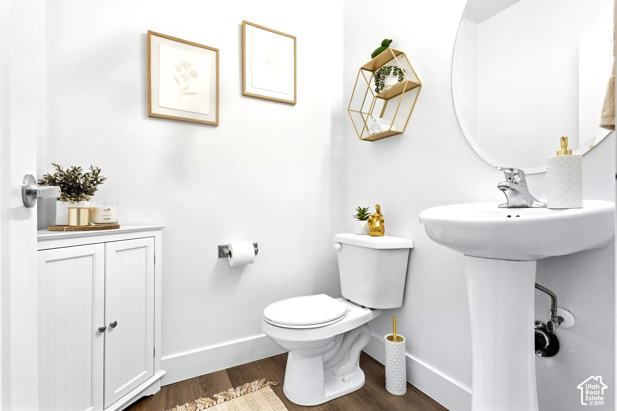 Pedestal sink, white toilet, wall-mounted hexagonal shelf, white storage cabinet, wood-finish flooring