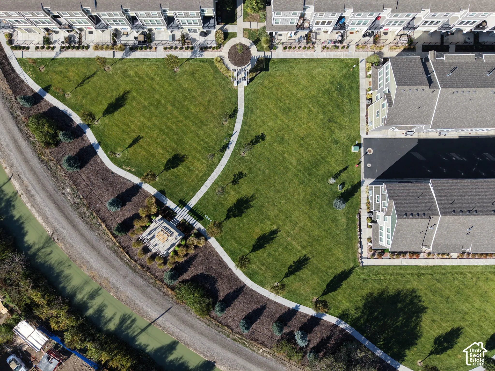 Expansive community greenspace featuring a manicured lawn, paved walking paths, and mature landscaping